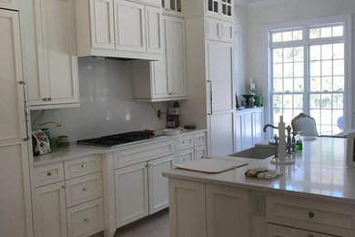 Example of a large classic brown floor kitchen design in Other with a farmhouse sink, beaded inset cabinets, white cabinets, quartz countertops, gray backsplash, stone slab backsplash, stainless steel appliances, an island and white countertops