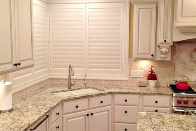 Exempel på ett avskilt, mellanstort klassiskt l-kök, med en undermonterad diskho, luckor med upphöjd panel, vita skåp, granitbänkskiva, beige stänkskydd, stänkskydd i keramik, rostfria vitvaror, mörkt trägolv, en köksö och brunt golv