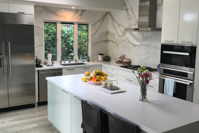 Inspiration for a mid-sized modern u-shaped medium tone wood floor and brown floor eat-in kitchen remodel in San Diego with a drop-in sink, flat-panel cabinets, white cabinets, quartz countertops, white backsplash, marble backsplash, stainless steel appliances and an island