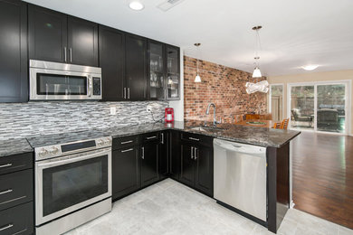 Enclosed kitchen - mid-sized transitional l-shaped porcelain tile enclosed kitchen idea in DC Metro with an undermount sink, shaker cabinets, black cabinets, quartzite countertops, gray backsplash, glass tile backsplash, stainless steel appliances and a peninsula