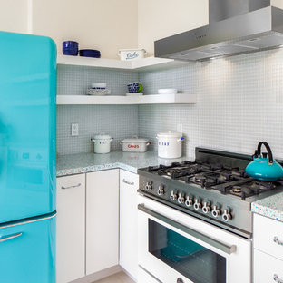 This is an example of a small eclectic u-shaped eat-in kitchen in San Francisco with a farmhouse sink, flat-panel cabinets, white cabinets, recycled glass benchtops, blue splashback, glass sheet splashback and porcelain floors.
