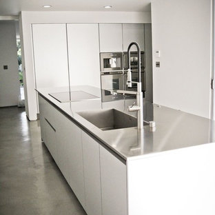 Inspiration for a large midcentury galley separate kitchen in Los Angeles with an integrated sink, flat-panel cabinets, white cabinets, stainless steel benchtops, stainless steel appliances, concrete floors, with island and grey floor.