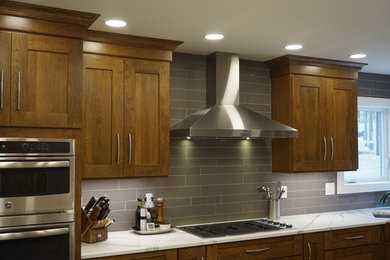 This is an example of a modern l-shaped kitchen/diner in Denver with a submerged sink, shaker cabinets, dark wood cabinets, engineered stone countertops, grey splashback, porcelain splashback, stainless steel appliances, medium hardwood flooring, an island, brown floors and white worktops.