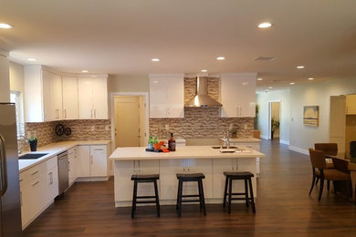 Photo of a traditional kitchen in Los Angeles with a submerged sink, flat-panel cabinets, white cabinets, engineered stone countertops, beige splashback, glass tiled splashback, stainless steel appliances, medium hardwood flooring, an island and brown floors.