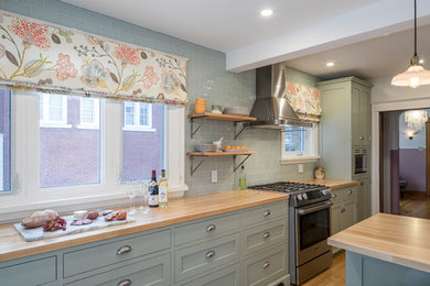 Mid-sized farmhouse galley medium tone wood floor eat-in kitchen photo in Ottawa with a farmhouse sink, recessed-panel cabinets, green cabinets, wood countertops, green backsplash, glass tile backsplash, stainless steel appliances and an island