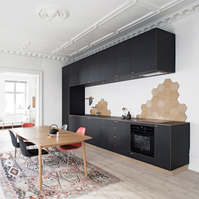 Eat-in kitchen - large scandinavian single-wall light wood floor eat-in kitchen idea in Copenhagen with flat-panel cabinets, black cabinets, beige backsplash, black appliances, no island, a drop-in sink and wood countertops