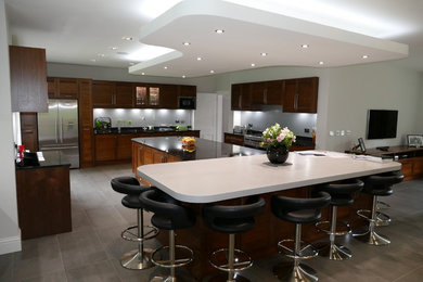 This is an example of a large traditional open plan kitchen in Buckinghamshire with a submerged sink, shaker cabinets, dark wood cabinets, granite worktops, grey splashback, glass sheet splashback, stainless steel appliances, porcelain flooring, an island and grey floors.