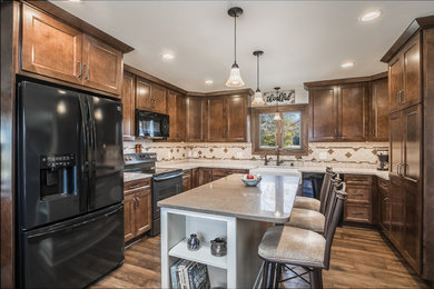 Example of a classic medium tone wood floor and brown floor kitchen design in Milwaukee with recessed-panel cabinets, dark wood cabinets, quartzite countertops, beige backsplash, mosaic tile backsplash, black appliances, an island and a farmhouse sink
