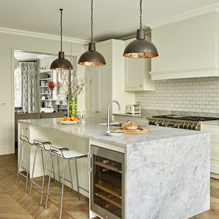 Inspiration for a classic galley kitchen in London with a submerged sink, shaker cabinets, white cabinets, white splashback, metro tiled splashback, stainless steel appliances, medium hardwood flooring, an island, brown floors and grey worktops.
