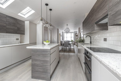 This is an example of a medium sized contemporary galley open plan kitchen in London with a single-bowl sink, flat-panel cabinets, dark wood cabinets, granite worktops, white splashback, metro tiled splashback, black appliances, medium hardwood flooring, an island, grey floors and beige worktops.