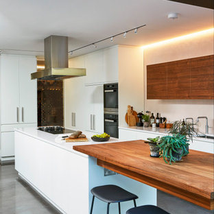 Photo of a contemporary l-shaped kitchen in London with a submerged sink, flat-panel cabinets, white cabinets, stainless steel appliances, concrete flooring, an island, grey floors and white worktops.