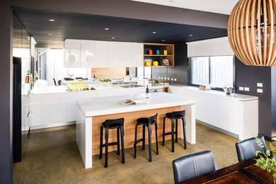 Photo of a medium sized contemporary u-shaped kitchen/diner in Melbourne with flat-panel cabinets, white cabinets, mirror splashback, stainless steel appliances, concrete flooring and an island.