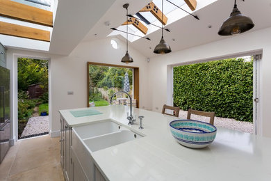 Country limestone floor and beige floor kitchen photo in London with a farmhouse sink, recessed-panel cabinets, green cabinets, solid surface countertops, white backsplash, ceramic backsplash, stainless steel appliances, an island and white countertops