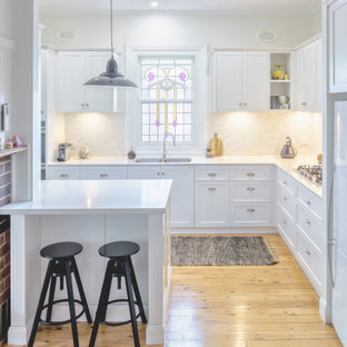 Design ideas for a mid-sized transitional galley eat-in kitchen in Newcastle - Maitland with an undermount sink, shaker cabinets, white cabinets, quartz benchtops, grey splashback, cement tile splashback, white appliances, light hardwood floors, with island, beige floor and white benchtop.