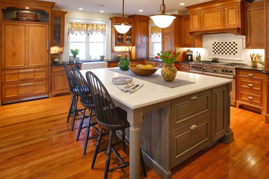 Example of a large classic l-shaped medium tone wood floor enclosed kitchen design in New York with a farmhouse sink, beaded inset cabinets, medium tone wood cabinets, quartzite countertops, white backsplash, ceramic backsplash, paneled appliances and an island