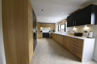 This is an example of a large modern l-shaped kitchen/diner in Kent with a double-bowl sink, flat-panel cabinets, light wood cabinets, quartz worktops, white splashback, glass sheet splashback, stainless steel appliances, vinyl flooring, no island and beige floors.