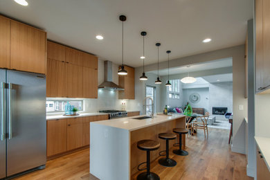 Inspiration for a mid-sized contemporary u-shaped medium tone wood floor enclosed kitchen remodel in Nashville with light wood cabinets, white backsplash, stainless steel appliances and an island