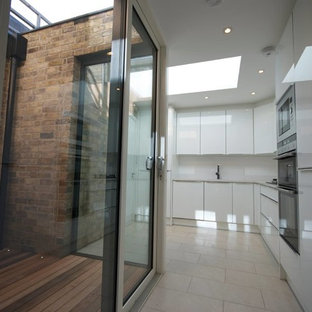 This is an example of a mid-sized modern galley eat-in kitchen in Dublin with an integrated sink, flat-panel cabinets, white cabinets, laminate benchtops, cement tile splashback, panelled appliances and ceramic floors.