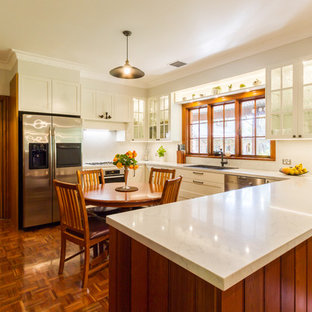 Design ideas for a mid-sized traditional u-shaped eat-in kitchen in Melbourne with a drop-in sink, shaker cabinets, white cabinets, marble benchtops, white splashback, marble splashback, stainless steel appliances, medium hardwood floors, a peninsula, brown floor and white benchtop.
