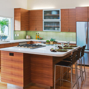 Foto di una cucina minimalista con elettrodomestici in acciaio inossidabile, ante lisce, ante in legno scuro, paraspruzzi verde, lavello sottopiano, top in superficie solida, parquet chiaro, isola e paraspruzzi con piastrelle di vetro