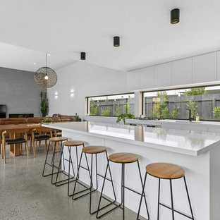 This is an example of a large contemporary galley open plan kitchen in Geelong with a double-bowl sink, flat-panel cabinets, white cabinets, quartz benchtops, window splashback, stainless steel appliances, concrete floors, with island, white benchtop and grey floor.