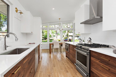 Mid-sized trendy galley light wood floor and brown floor eat-in kitchen photo in Other with a single-bowl sink, flat-panel cabinets, medium tone wood cabinets, quartz countertops, white backsplash, subway tile backsplash, stainless steel appliances, no island and white countertops