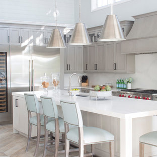 Idee per una cucina a L stile marinaro con lavello sottopiano, ante in stile shaker, ante grigie, paraspruzzi bianco, elettrodomestici in acciaio inossidabile, isola, pavimento beige e top bianco