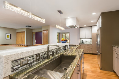 Example of a trendy light wood floor kitchen design in Detroit with an undermount sink, flat-panel cabinets, granite countertops, metallic backsplash, glass tile backsplash and stainless steel appliances