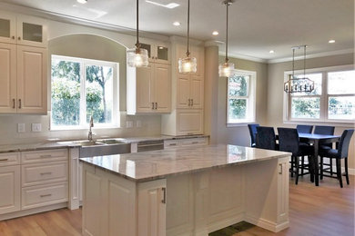 Eat-in kitchen - mid-sized transitional u-shaped porcelain tile eat-in kitchen idea in Miami with a farmhouse sink, raised-panel cabinets, white cabinets, quartzite countertops, subway tile backsplash, stainless steel appliances, an island and beige backsplash