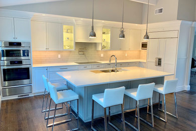 Example of a mid-sized transitional l-shaped dark wood floor and brown floor eat-in kitchen design in New York with a double-bowl sink, flat-panel cabinets, white cabinets, quartz countertops, beige backsplash, glass tile backsplash, stainless steel appliances, an island and white countertops