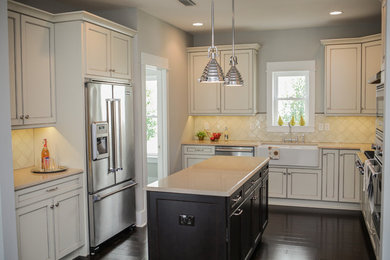 Amerikansk inredning av ett kök, med en rustik diskho, vita skåp, vitt stänkskydd, rostfria vitvaror, mörkt trägolv, en köksö och brunt golv