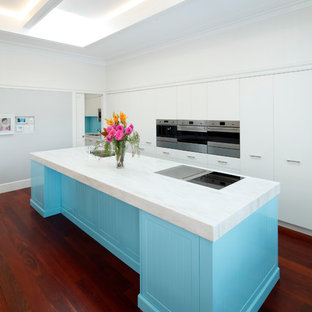 Large contemporary galley kitchen in Sydney with an undermount sink, blue cabinets, stainless steel appliances, dark hardwood floors, with island, red floor, white benchtop and flat-panel cabinets.