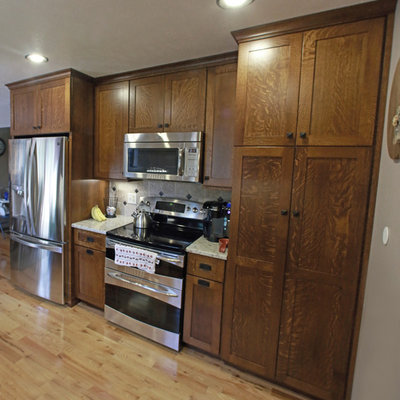 Small farmhouse l-shaped light wood floor and yellow floor eat-in kitchen photo in Other with a farmhouse sink, shaker cabinets, brown cabinets, granite countertops, beige backsplash, ceramic backsplash, stainless steel appliances and a peninsula