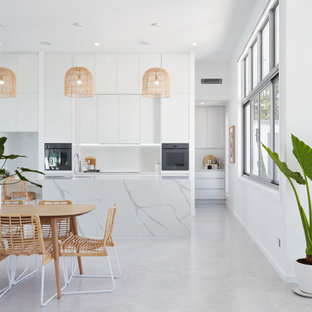 Contemporary u-shaped eat-in kitchen in Gold Coast - Tweed with flat-panel cabinets, white cabinets, white splashback, black appliances, with island, grey floor and grey benchtop.