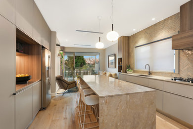 This is an example of a contemporary galley kitchen in Sydney with a submerged sink, flat-panel cabinets, grey cabinets, beige splashback, stainless steel appliances, light hardwood flooring, an island, beige floors and beige worktops.
