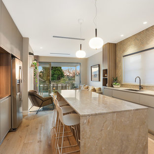 This is an example of a contemporary galley kitchen in Sydney with an undermount sink, flat-panel cabinets, grey cabinets, beige splashback, stainless steel appliances, light hardwood floors, with island, beige floor and beige benchtop.