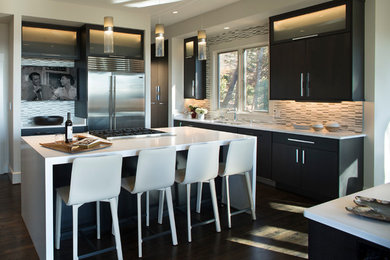Inspiration for a large modern dark wood floor enclosed kitchen remodel in Other with a single-bowl sink, glass-front cabinets, dark wood cabinets, solid surface countertops, multicolored backsplash, stone tile backsplash, stainless steel appliances and an island