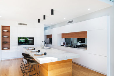 Moderne Küche in L-Form mit Unterbauwaschbecken, flächenbündigen Schrankfronten, weißen Schränken, schwarzen Elektrogeräten, braunem Holzboden, Kücheninsel, braunem Boden, weißer Arbeitsplatte und Marmor-Arbeitsplatte in Brisbane