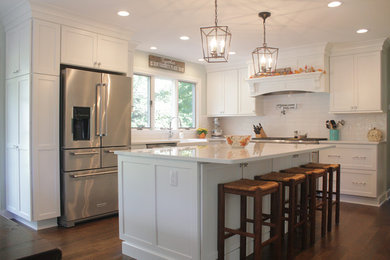 Inspiration for a mid-sized transitional l-shaped medium tone wood floor and brown floor eat-in kitchen remodel in Detroit with a farmhouse sink, shaker cabinets, white cabinets, quartz countertops, white backsplash, ceramic backsplash, stainless steel appliances, an island and white countertops