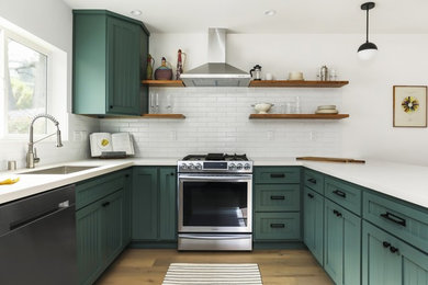 Inspiration for a transitional u-shaped light wood floor kitchen remodel in Los Angeles with an undermount sink, recessed-panel cabinets, green cabinets, white backsplash, subway tile backsplash, stainless steel appliances, a peninsula and white countertops