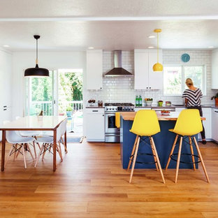Imagen de cocina comedor en L, actual, de tamaño medio, con fregadero bajoencimera, armarios con paneles lisos, puertas de armario blancas, encimera de cuarzo compacto, salpicadero blanco, salpicadero de azulejos tipo metro, electrodomésticos de acero inoxidable, suelo vinílico, una isla y suelo marrón