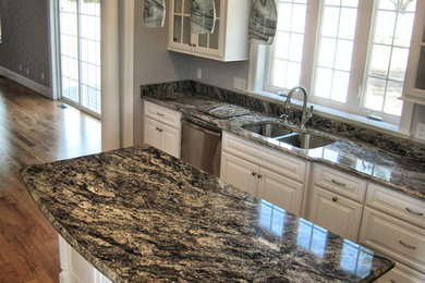 Open concept kitchen - modern medium tone wood floor open concept kitchen idea in Providence with an undermount sink, raised-panel cabinets, white cabinets, granite countertops, stone slab backsplash, stainless steel appliances and an island