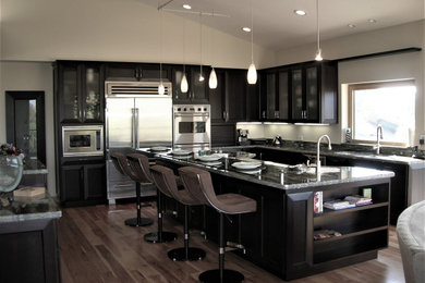 Contemporary l-shaped open plan kitchen in Los Angeles with a submerged sink, recessed-panel cabinets, dark wood cabinets, granite worktops, stainless steel appliances, light hardwood flooring, multiple islands, brown floors and green worktops.