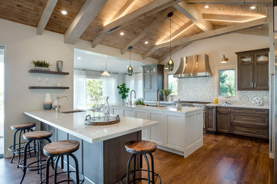 This is an example of a large farmhouse l-shaped open plan kitchen in Los Angeles with engineered stone countertops, multi-coloured splashback, stainless steel appliances, multiple islands, medium hardwood flooring, dark wood cabinets, cement tile splashback, brown floors, a submerged sink, white worktops and recessed-panel cabinets.