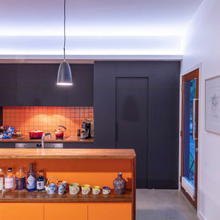 This is an example of a small contemporary galley open plan kitchen in Canberra - Queanbeyan with a drop-in sink, flat-panel cabinets, black cabinets, wood benchtops, orange splashback, porcelain splashback, stainless steel appliances, concrete floors, with island and grey floor.