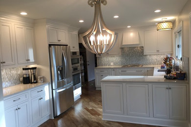Example of a mid-sized transitional u-shaped medium tone wood floor eat-in kitchen design in Chicago with an undermount sink, beaded inset cabinets, white cabinets, quartz countertops, blue backsplash, glass sheet backsplash, stainless steel appliances and a peninsula