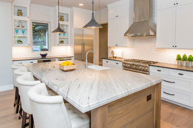 Example of a large cottage light wood floor eat-in kitchen design in Austin with a farmhouse sink, shaker cabinets, white cabinets, marble countertops, white backsplash, subway tile backsplash, stainless steel appliances and an island