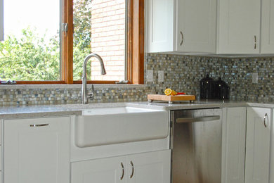 Aménagement d'une petite cuisine bord de mer en U fermée avec un placard à porte shaker, des portes de placard blanches, un plan de travail en quartz modifié, une péninsule, un plan de travail gris, un évier de ferme, une crédence multicolore, une crédence en carreau de verre, un électroménager en acier inoxydable, un sol en bois brun et un sol orange.