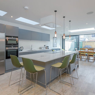 Inspiration for a medium sized contemporary single-wall kitchen/diner in London with a submerged sink, flat-panel cabinets, grey cabinets, stainless steel appliances, an island, beige floors and white worktops.