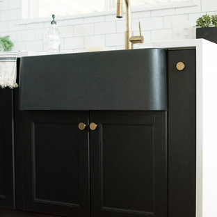 Medium sized farmhouse u-shaped kitchen/diner in Other with a belfast sink, shaker cabinets, black cabinets, engineered stone countertops, white splashback, metro tiled splashback, stainless steel appliances, porcelain flooring, no island, grey floors and white worktops.